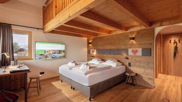 A bedroom with a large bed, wooden ceiling beams, a desk with a chair, and a window with curtains.