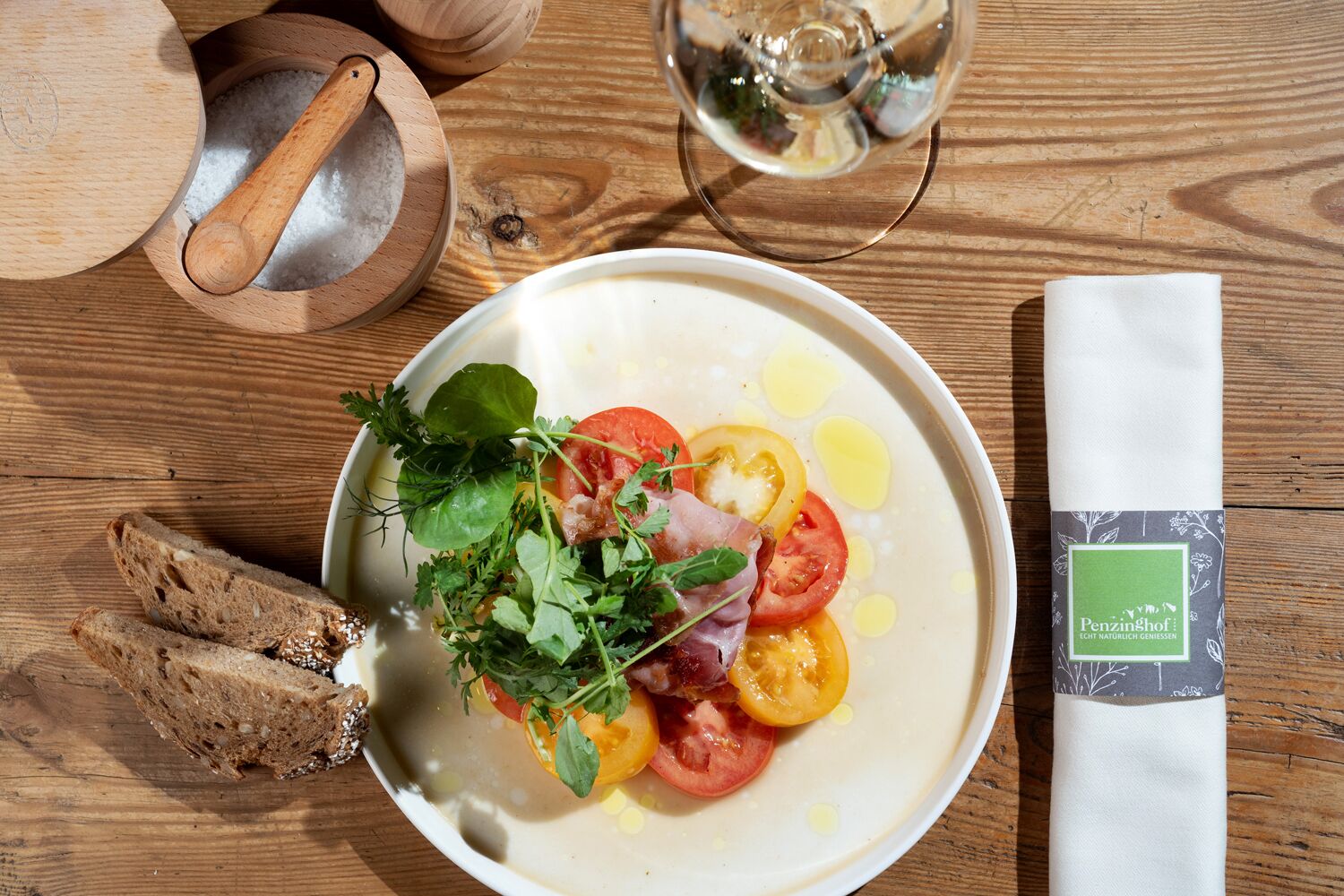 A plate of food with tomatoes, herbs, and a drizzle of olive oil, accompanied by slices of bread and a napkin with a green label.