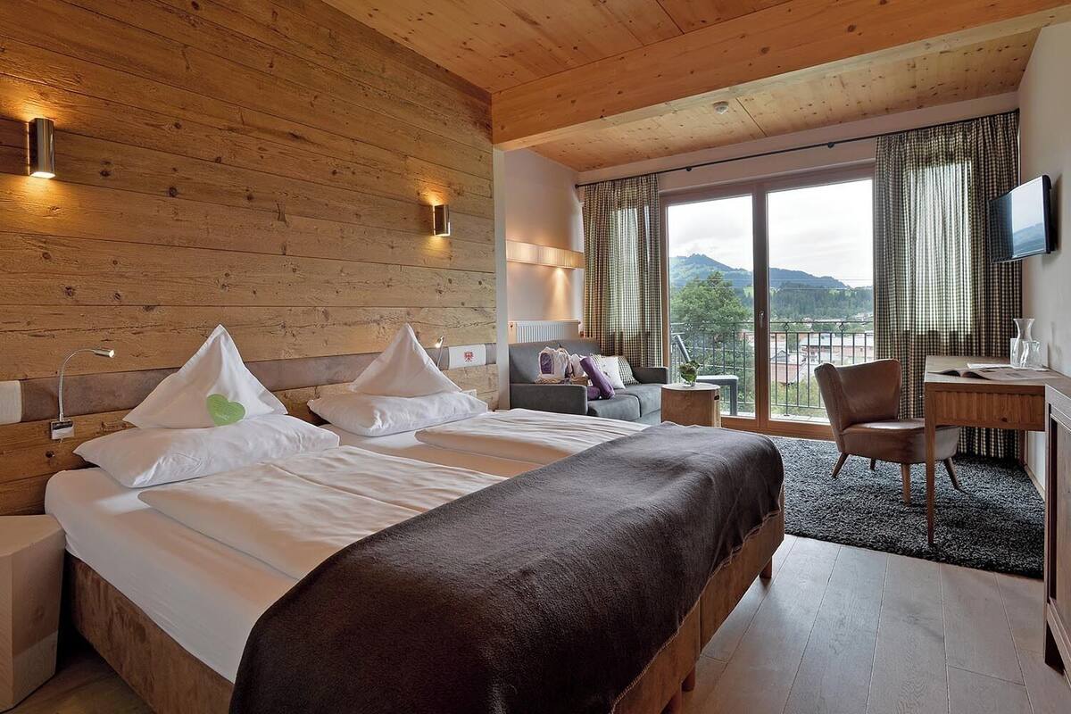 A hotel room with a wooden interior, a large bed with white linens, a desk with a chair, and a view of the outdoors.