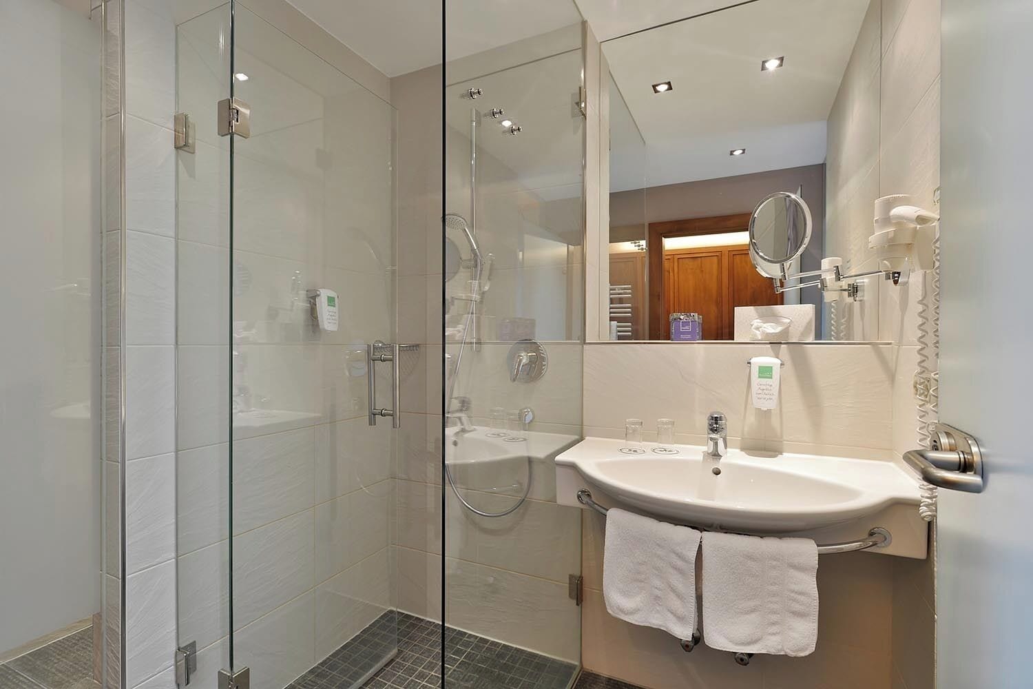 A modern bathroom with a glass-enclosed shower, a white sink with a mirror, and a towel rack.