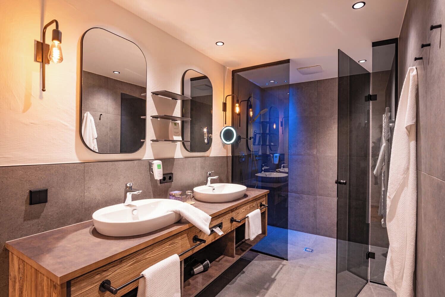 A modern bathroom with two sinks, a large mirror, and a glass shower enclosure.