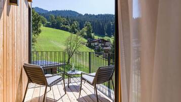 Eine Holzterrasse mit zwei Stühlen und einem Tisch, mit Blick auf ein grünes Tal und Häuser.