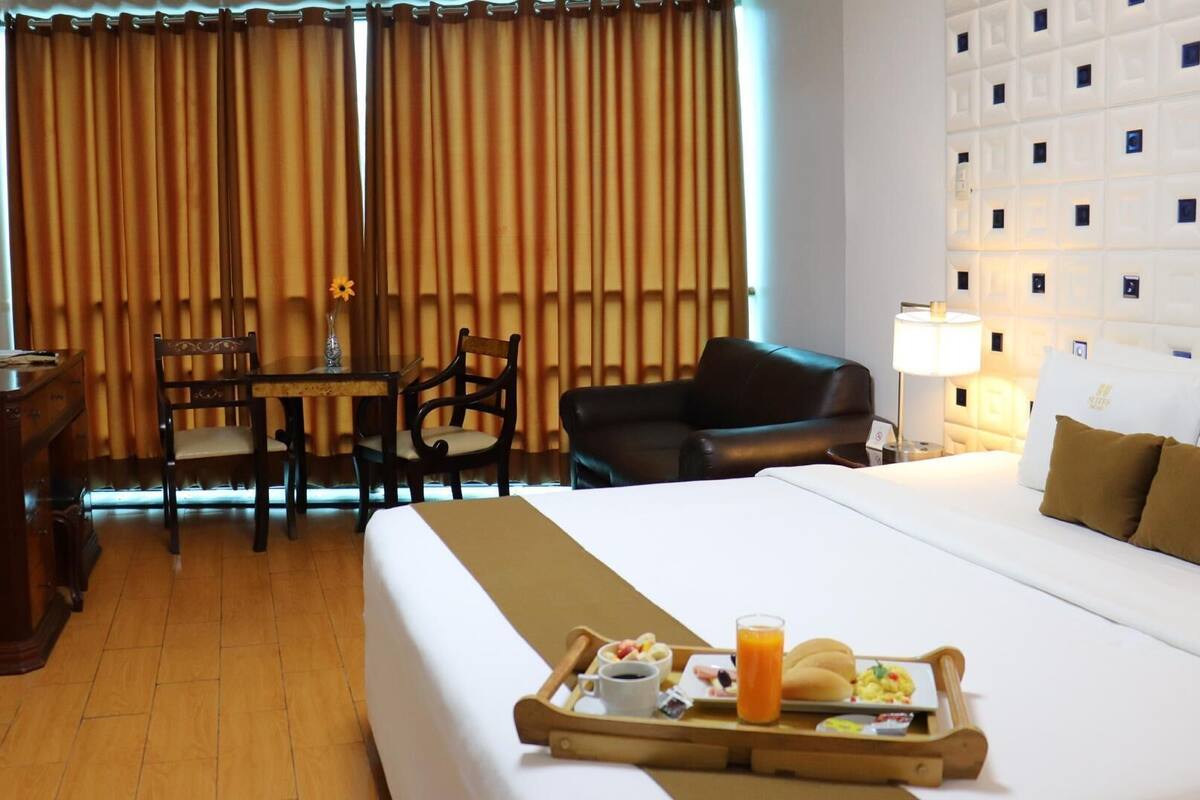Una habitación de hotel con cama, una mesa de comedor con sillas, un sofá, un escritorio y una bandeja con alimentos para el desayuno.