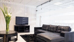 A modern living room with a black leather sofa, a glass coffee table, a flat-screen TV, and a marble wall.