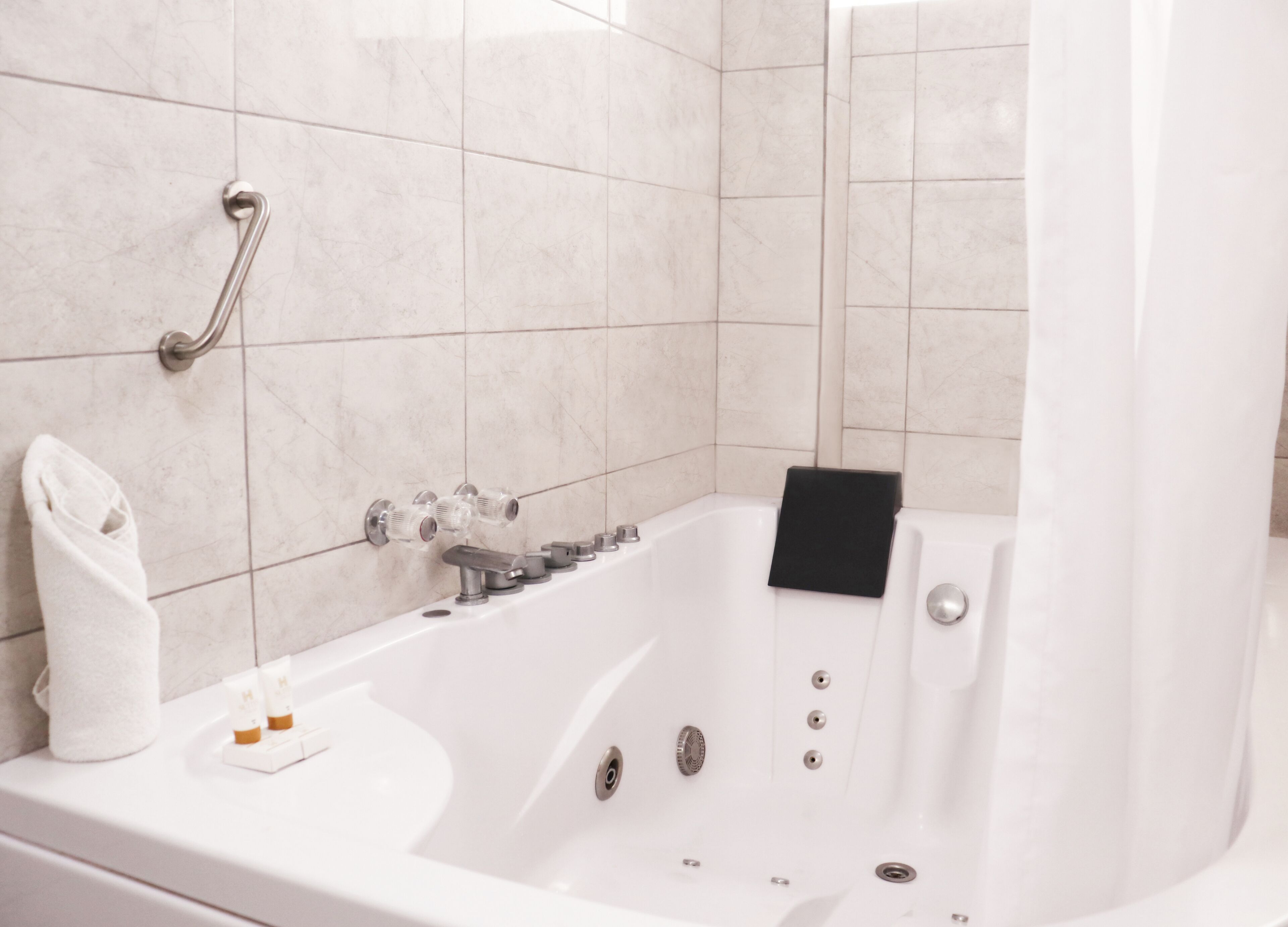 A modern bathroom with a white bathtub, a handheld showerhead, and a towel rack.