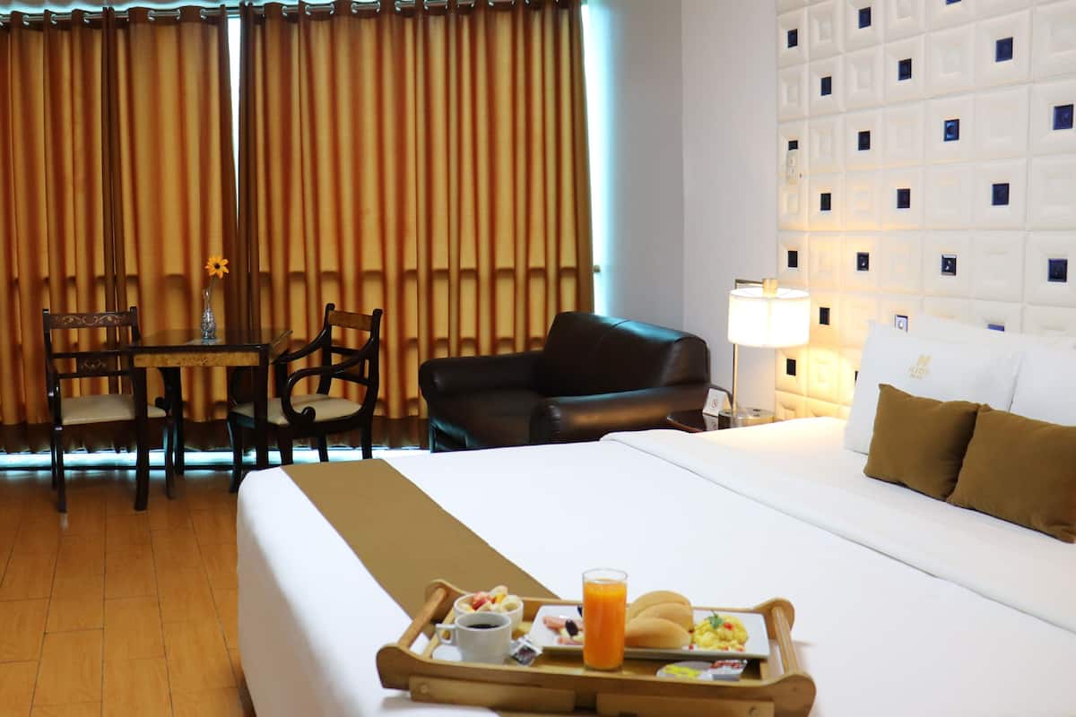 Una habitación de hotel con cama, una mesa de comedor con sillas, un sofá y una bandeja con alimentos para el desayuno.