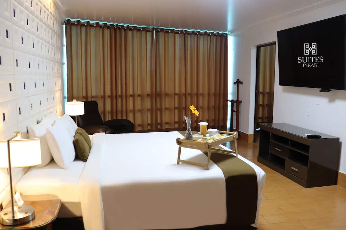 Una habitación de hotel con cama, mesita de noche, lámpara, televisión y televisor de pared.