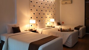A hotel room with two beds, a wall with a geometric pattern, a bedside table with a lamp, and a vase with a flower.