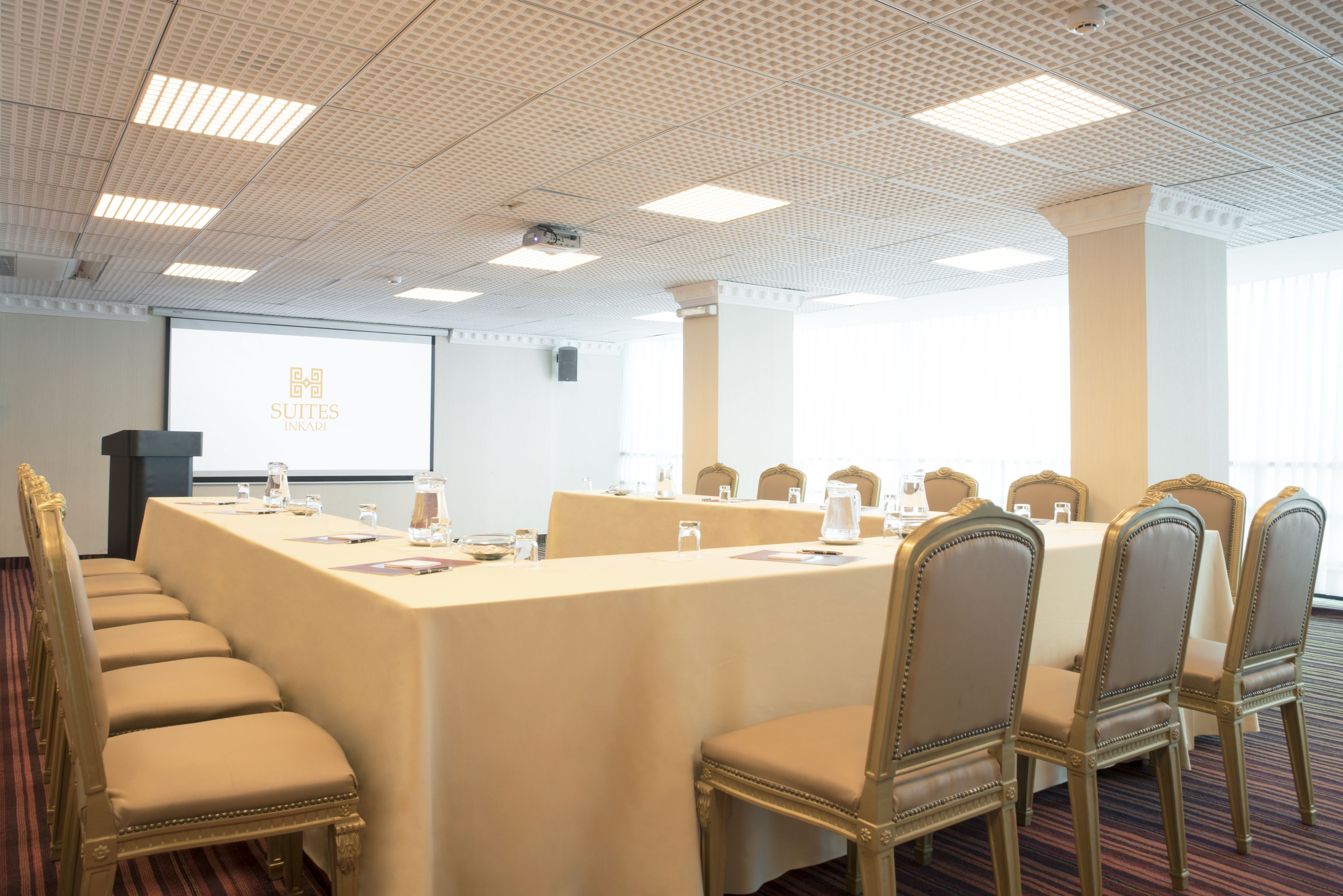Un salón de conferencias con una mesa larga, sillas y una pantalla proyectora mostrando "SUTTES INKATI".