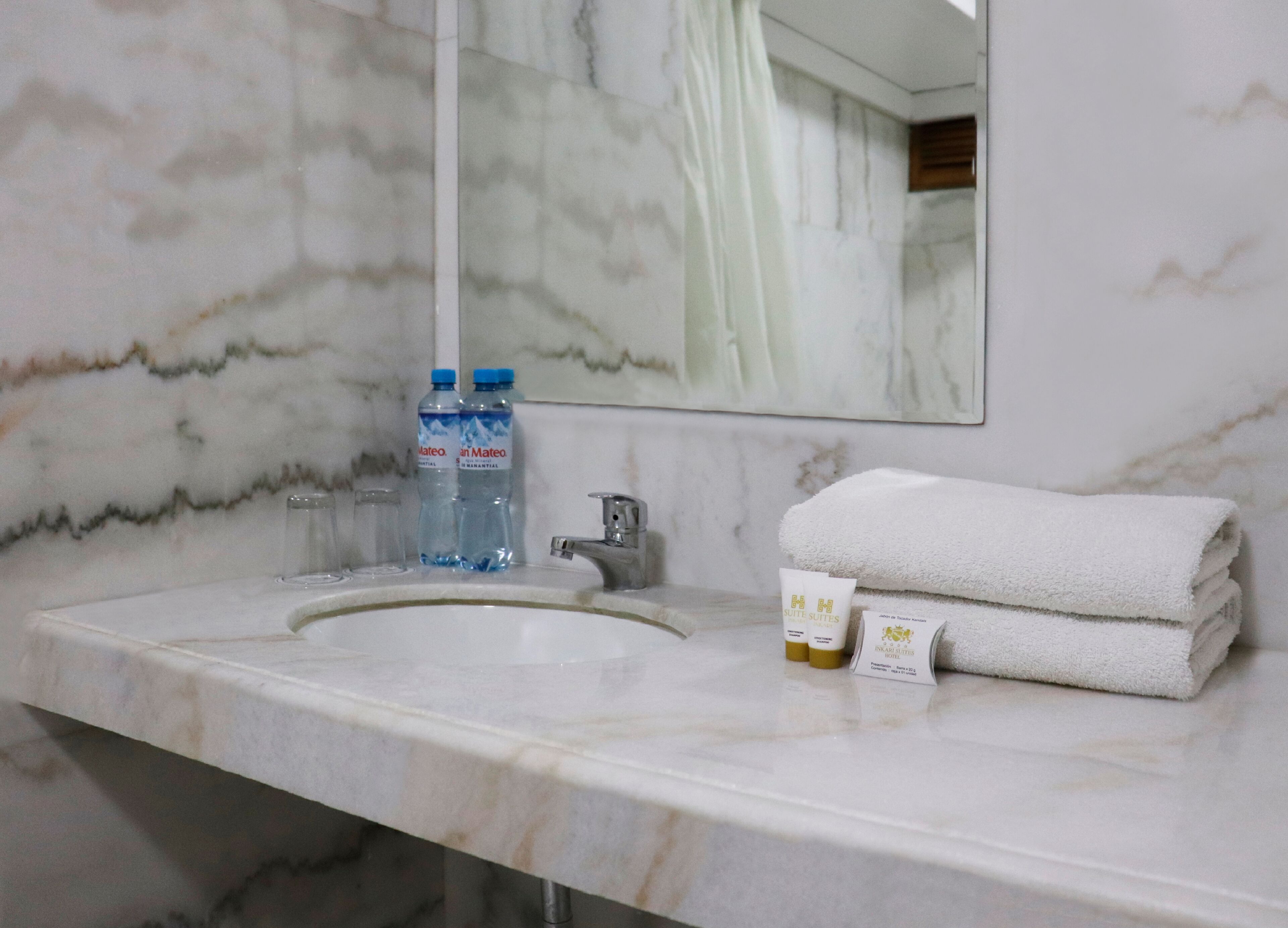 Un baño con lavamanos de mármol, dos botellas de agua, una toalla y artículos de aseo.
