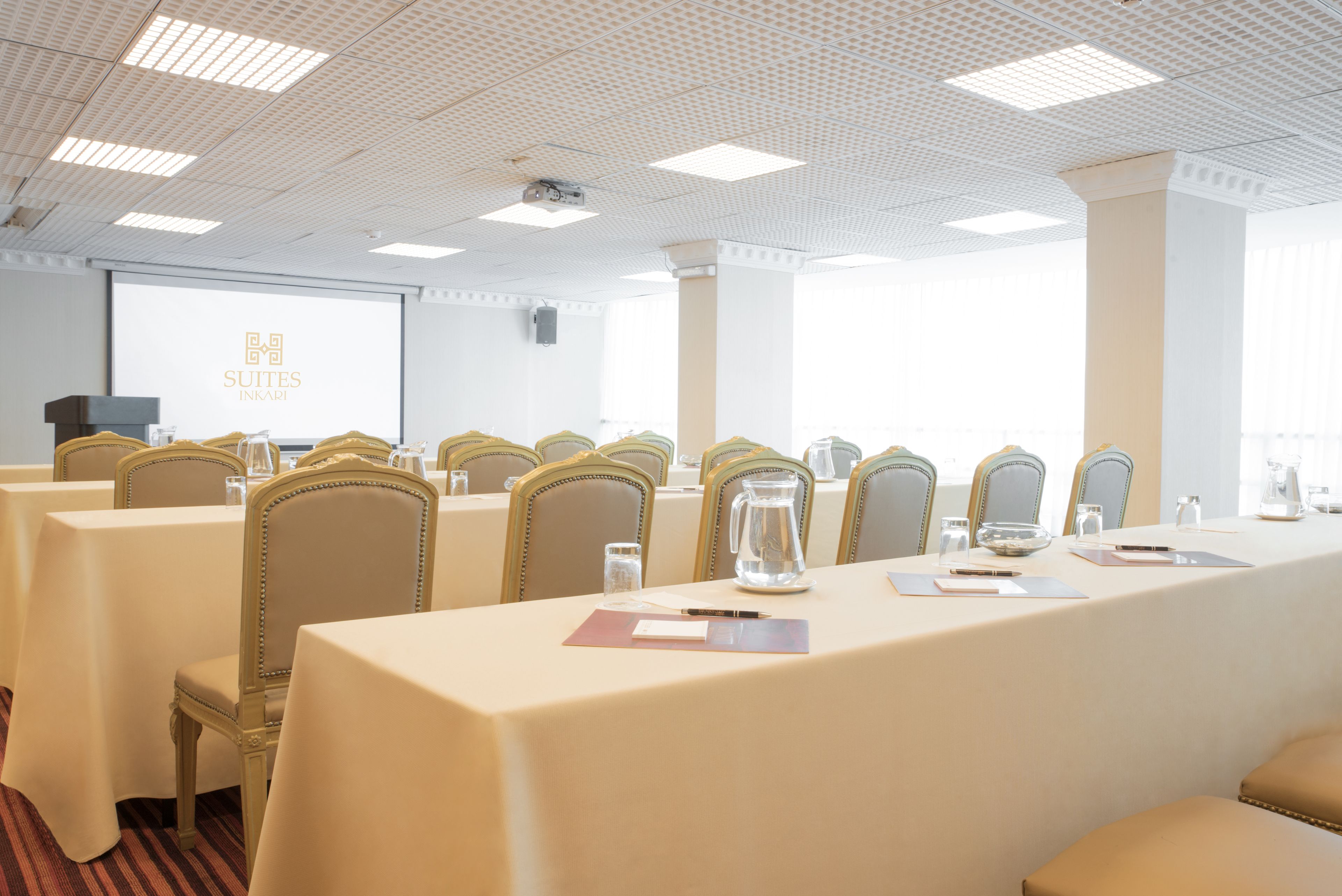 Ein Konferenzraum mit mehreren Tischen und Stühlen, einer Projektionsleinwand und einer Präsentation an der Wand.