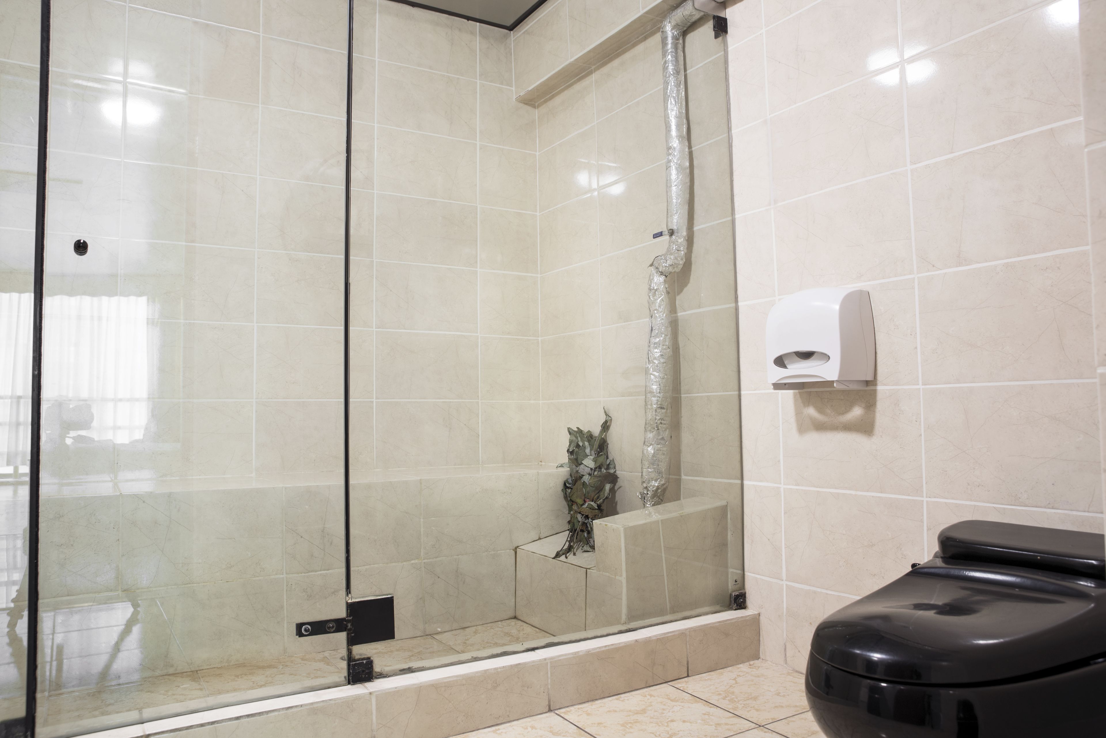 A modern bathroom with a glass-enclosed shower, a toilet, and a hand dryer.