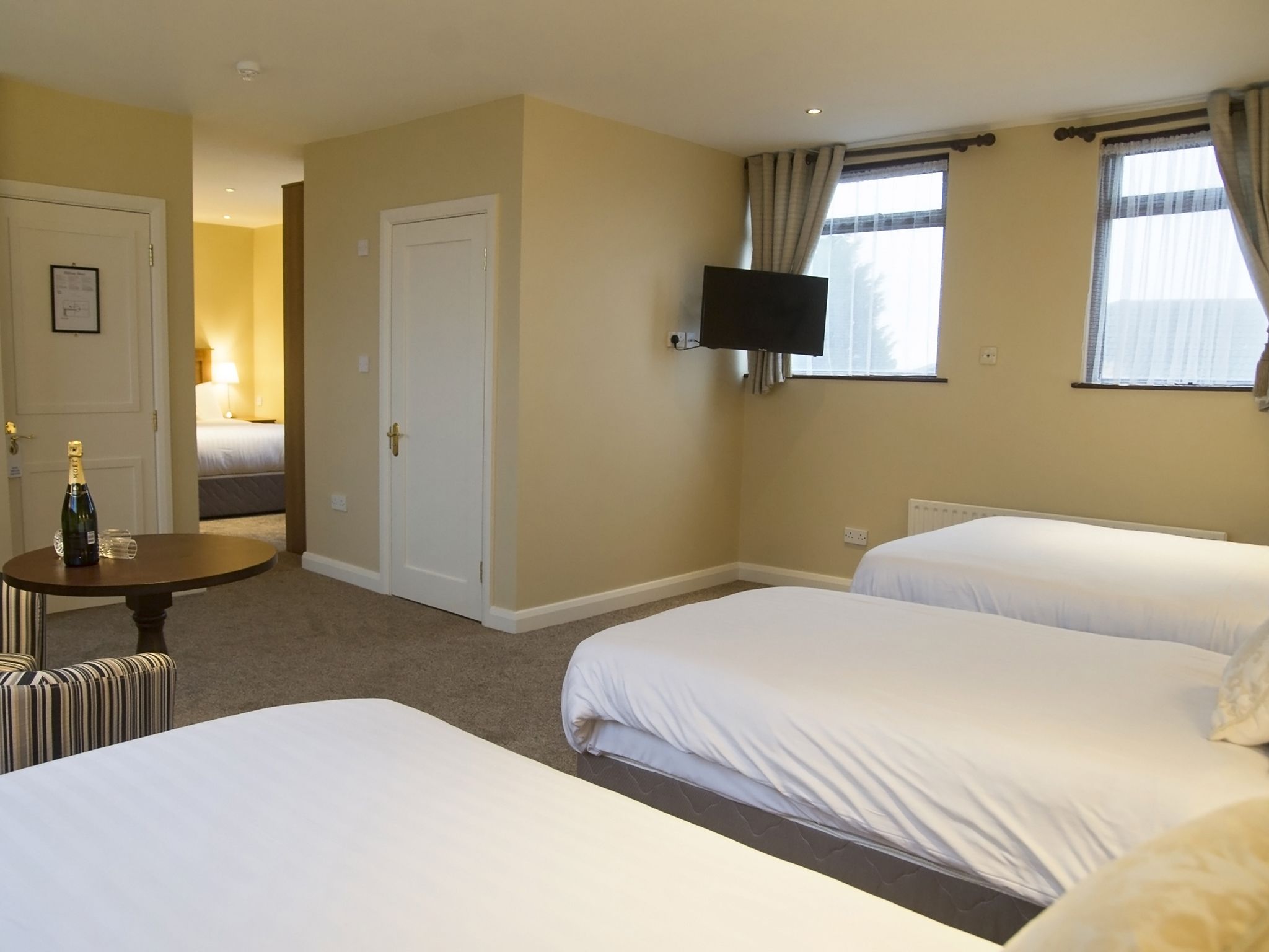 A hotel room with two beds, a television mounted on the wall, and a small table with a bottle and glass.