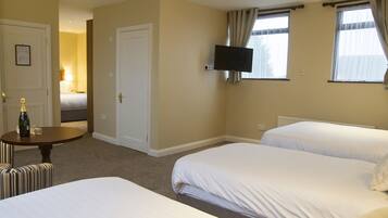 A hotel room with two beds, a television mounted on the wall, and a small table with a bottle and glass.