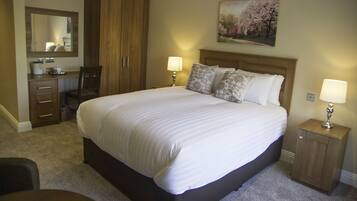 A bedroom with a large bed, two bedside tables with lamps, a wooden wardrobe, a desk with a chair, and a mirror.