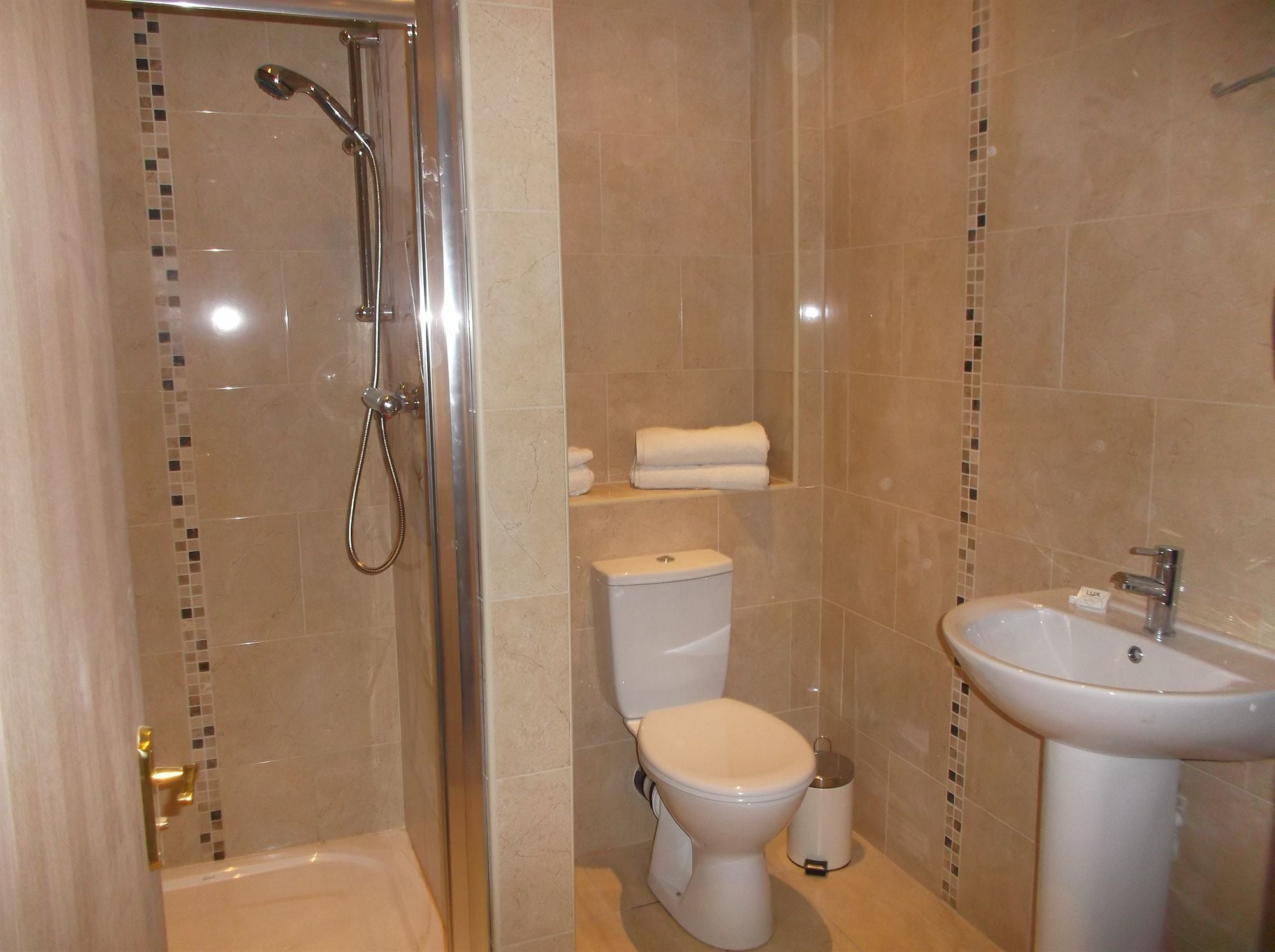 A bathroom with a glass-enclosed shower, a toilet, a sink, and a small shelf with towels.