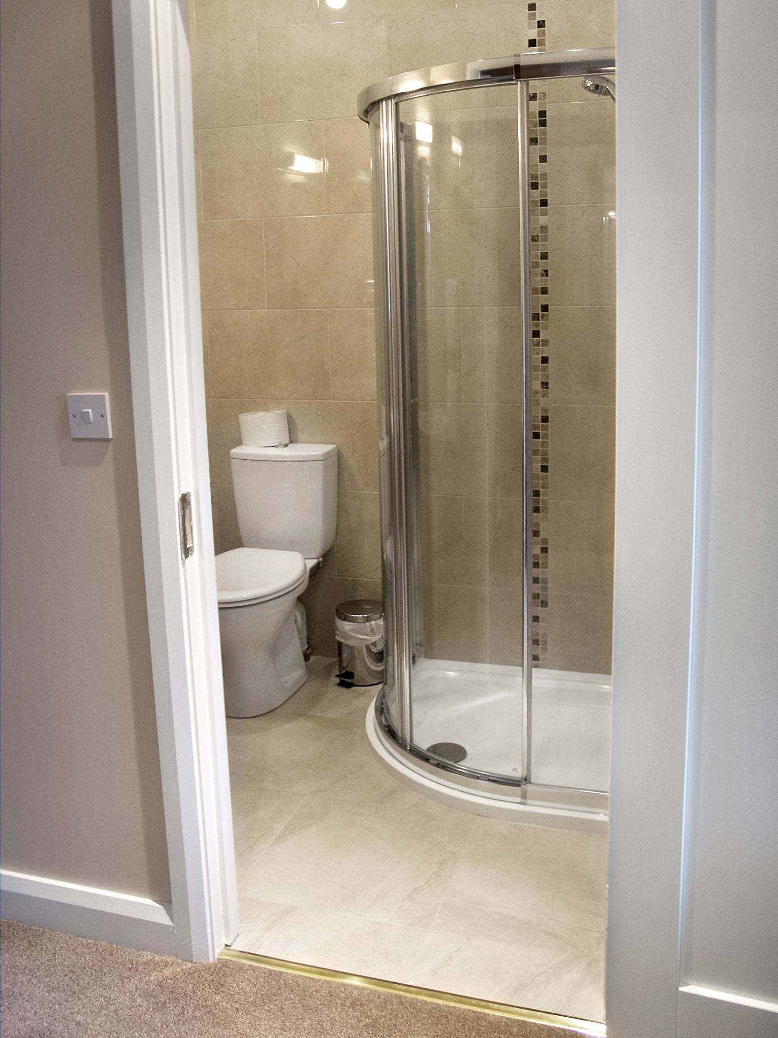A modern bathroom with a glass-enclosed shower, a toilet, and a trash bin.