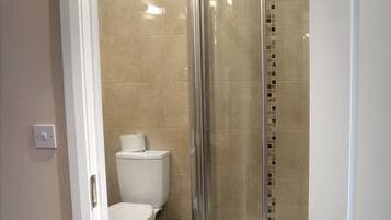 A modern bathroom with a glass-enclosed shower, a toilet, and a trash bin.