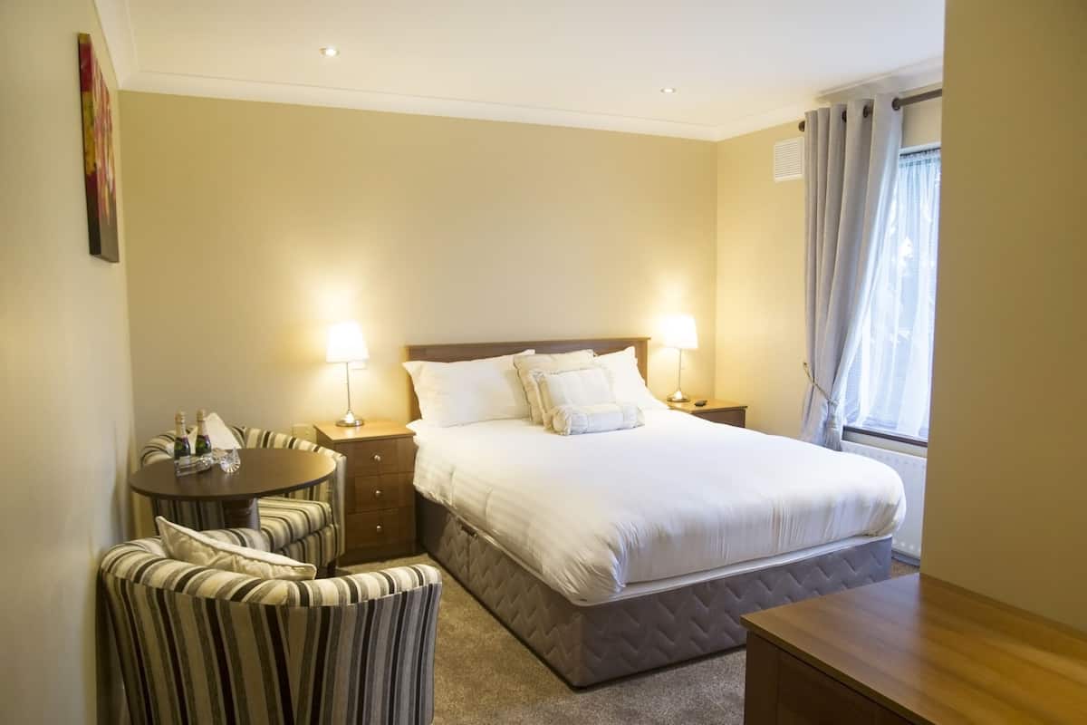 Une chambre d’hôtel avec un grand lit, deux tables de chevet avec des lampes, une petite table ronde avec des chaises et une fenêtre avec des rideaux.
