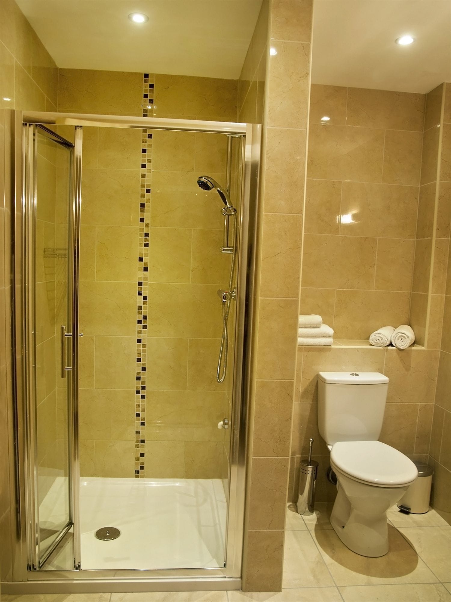 A modern bathroom with a glass-enclosed shower, a toilet, and a shelf with towels.