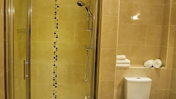 A modern bathroom with a glass-enclosed shower, a toilet, and a shelf with towels.