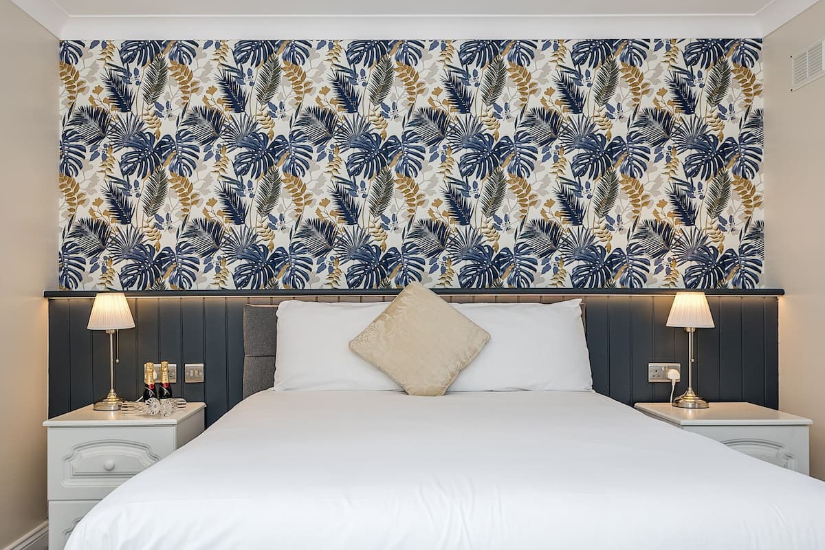Une chambre d’hôtel avec un grand lit, deux tables de chevet et une tête de lit ornée d’un motif de feuilles tropicales.