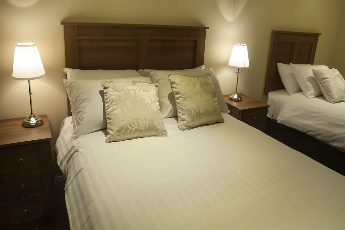 Une chambre d’hôtel avec deux lits, chacun doté d’une tête de lit en bois, de draps blancs et de deux lampes de chevet.