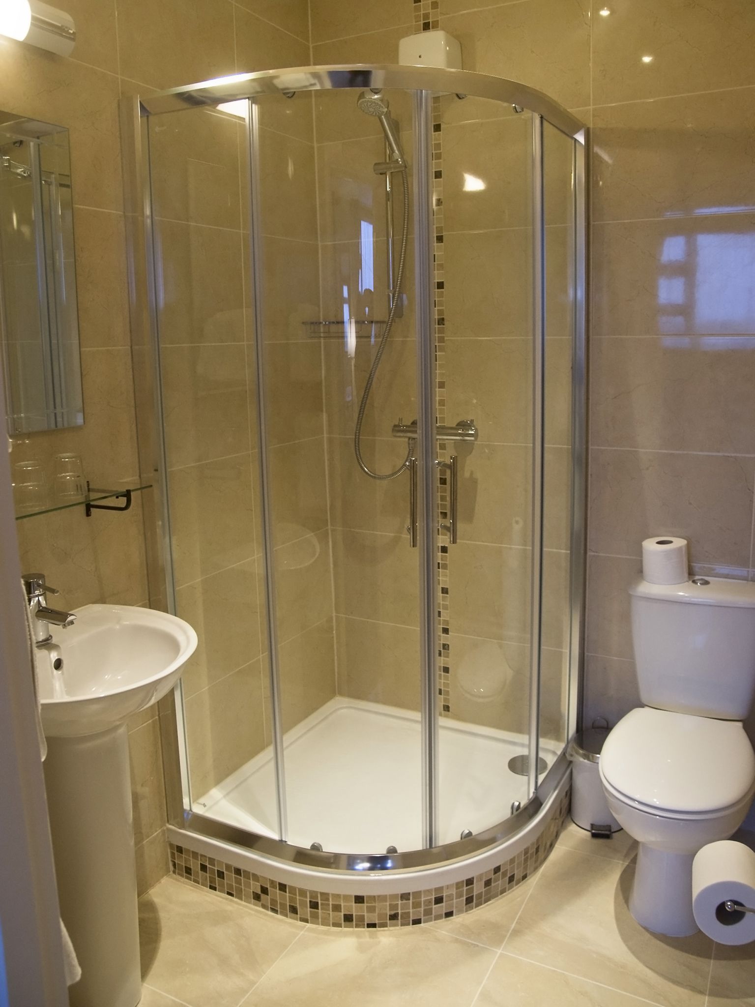A glass-enclosed shower with a handheld showerhead and a wall-mounted faucet.
