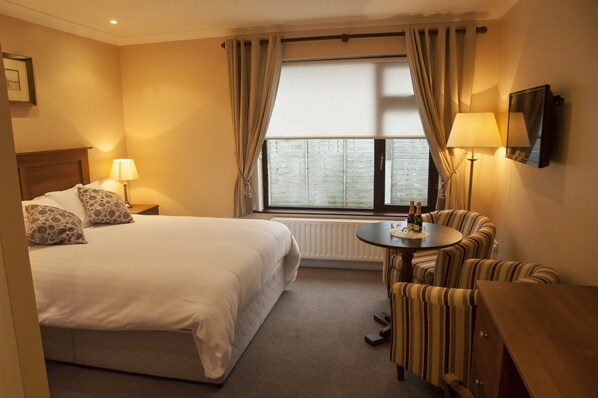 A hotel room with a bed, a small round table with bottles, a sofa, and a TV on the wall.