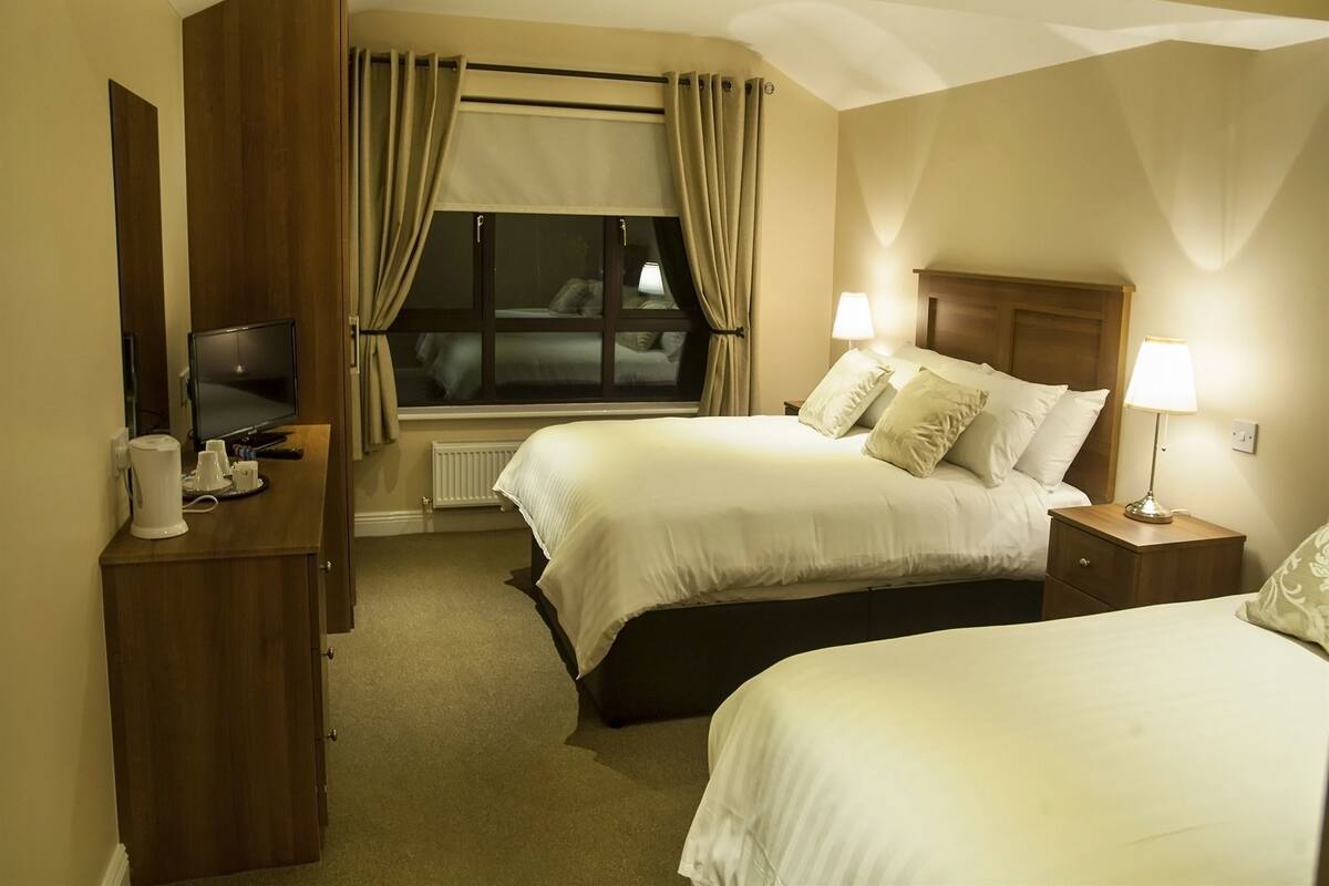 Une chambre d’hôtel avec deux lits, une télévision, un bureau avec une machine à café et une fenêtre avec des rideaux.