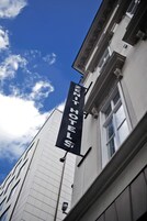 Μια πινακίδα ξενοδοχείου με την επιγραφή «ΝΕΟ ΞΕΝΟΔΟΧΕΙΟ», σε φόντο έναν καθαρό, γαλάζιο ουρανό.