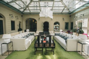 A spacious lounge area with a high ceiling and glass panels, featuring a central coffee table, white sofas, and a green carpet. - Hotel Zenit Budapest Palace (Budapest)