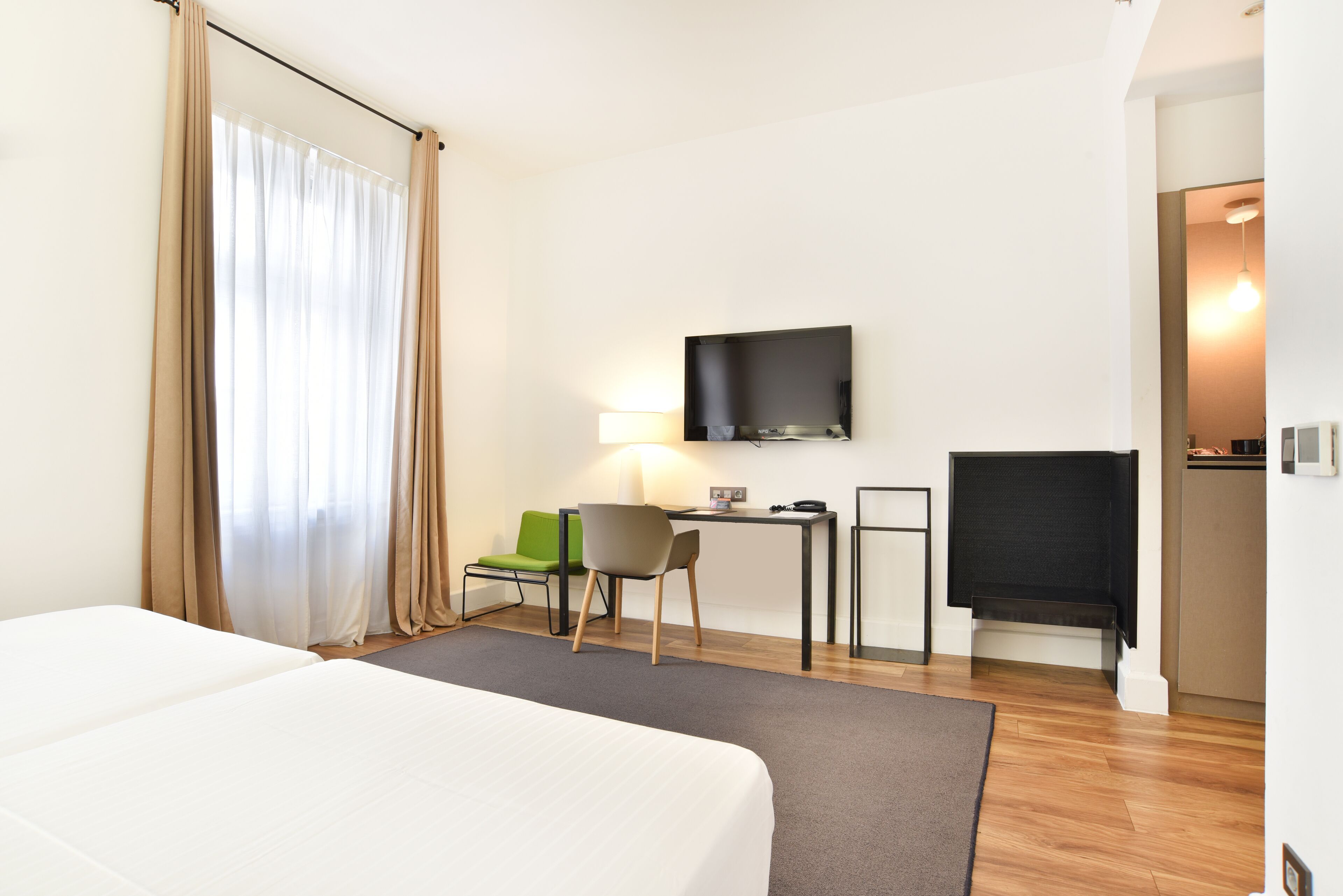 A hotel room with a bed, a desk, a chair, a television, and a window with curtains.