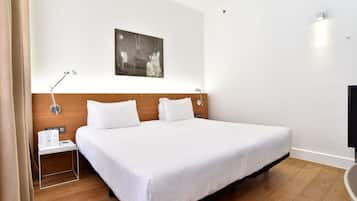 Quarto de hotel com uma cama grande, cabeceira de madeira, mesa de cabeceira com abajur e uma obra de arte na parede.