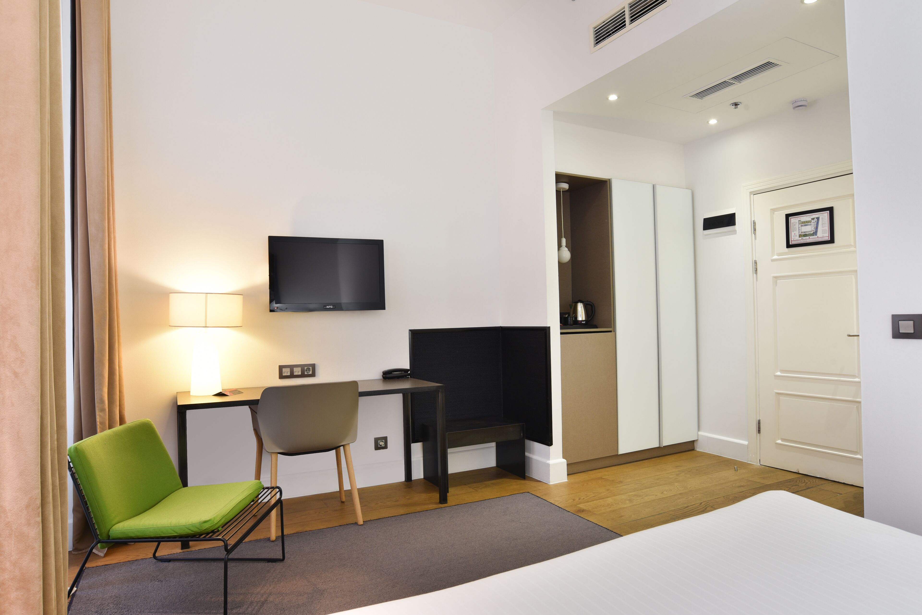 A hotel room with a bed, a desk with a chair, a TV, and a door.