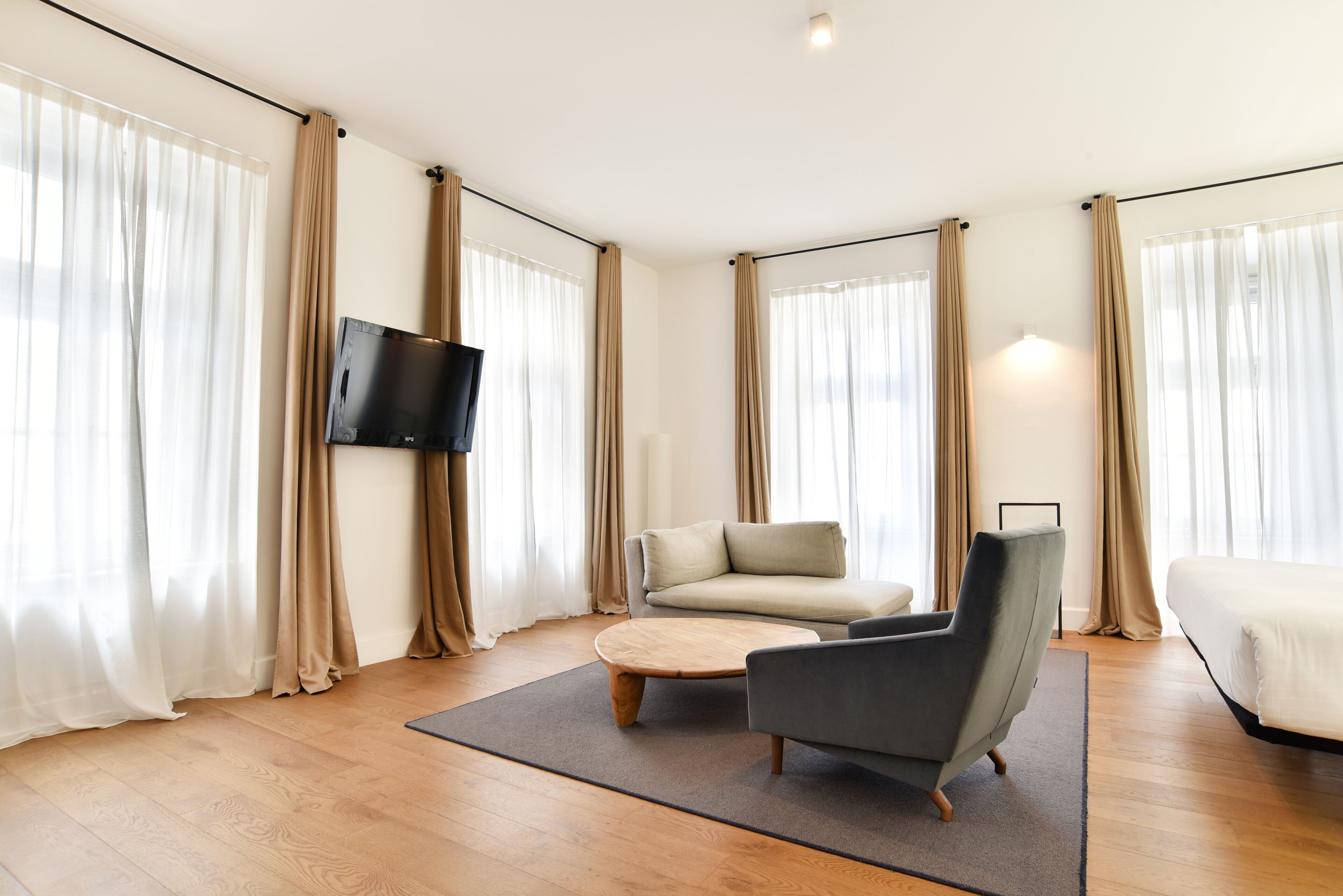 A modern living room with a sofa, armchair, coffee table, and a flat-screen TV mounted on the wall.