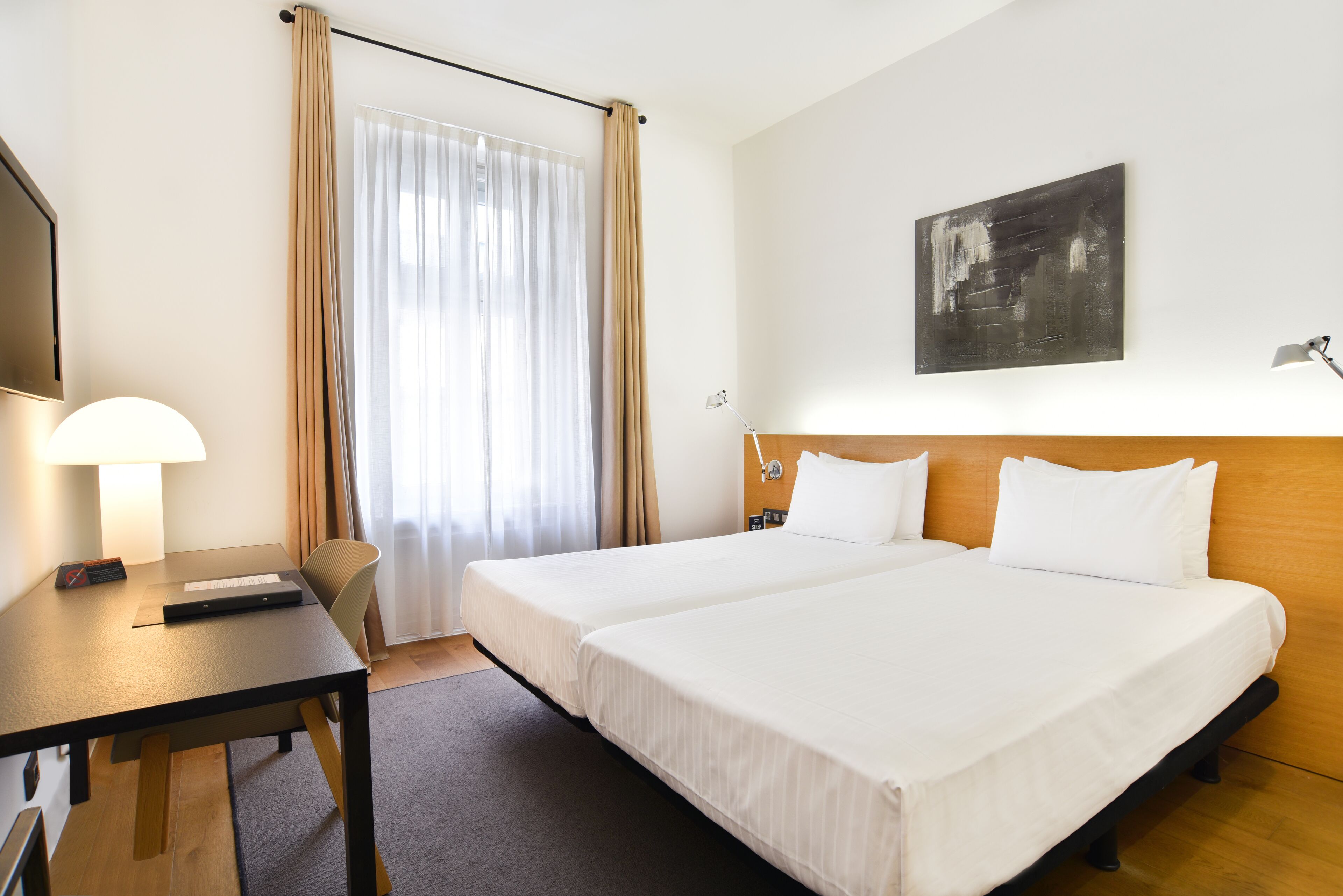 Een hotelkamer met twee bedden, een bureau, een stoel, een lamp en een schilderij aan de muur.