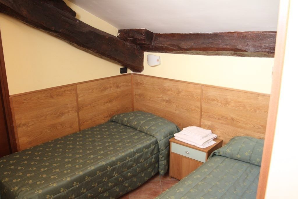 Una stanza piccola e accogliente con due letti singoli, una testiera in legno e un comodino in legno con una lampada.