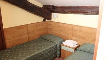 Una stanza piccola e accogliente con due letti singoli, una testiera in legno e un comodino in legno con una lampada.