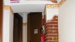 A hallway with a fire extinguisher mounted on the wall, a door, and a vase with dried plants. - Hotel Cavallo Bianco (Novara)
