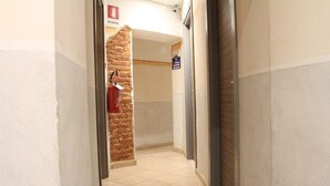 A narrow hallway with a tiled floor, a brick wall, and a fire extinguisher on the left. - Hotel Cavallo Bianco (Novara)