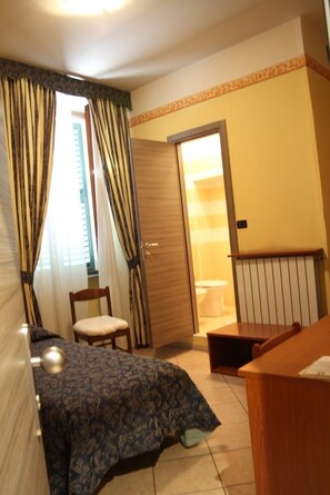 A bedroom with a bed, a chair, a desk, a wardrobe, and a bathroom visible through an open door. - Hotel Cavallo Bianco (Novara)
