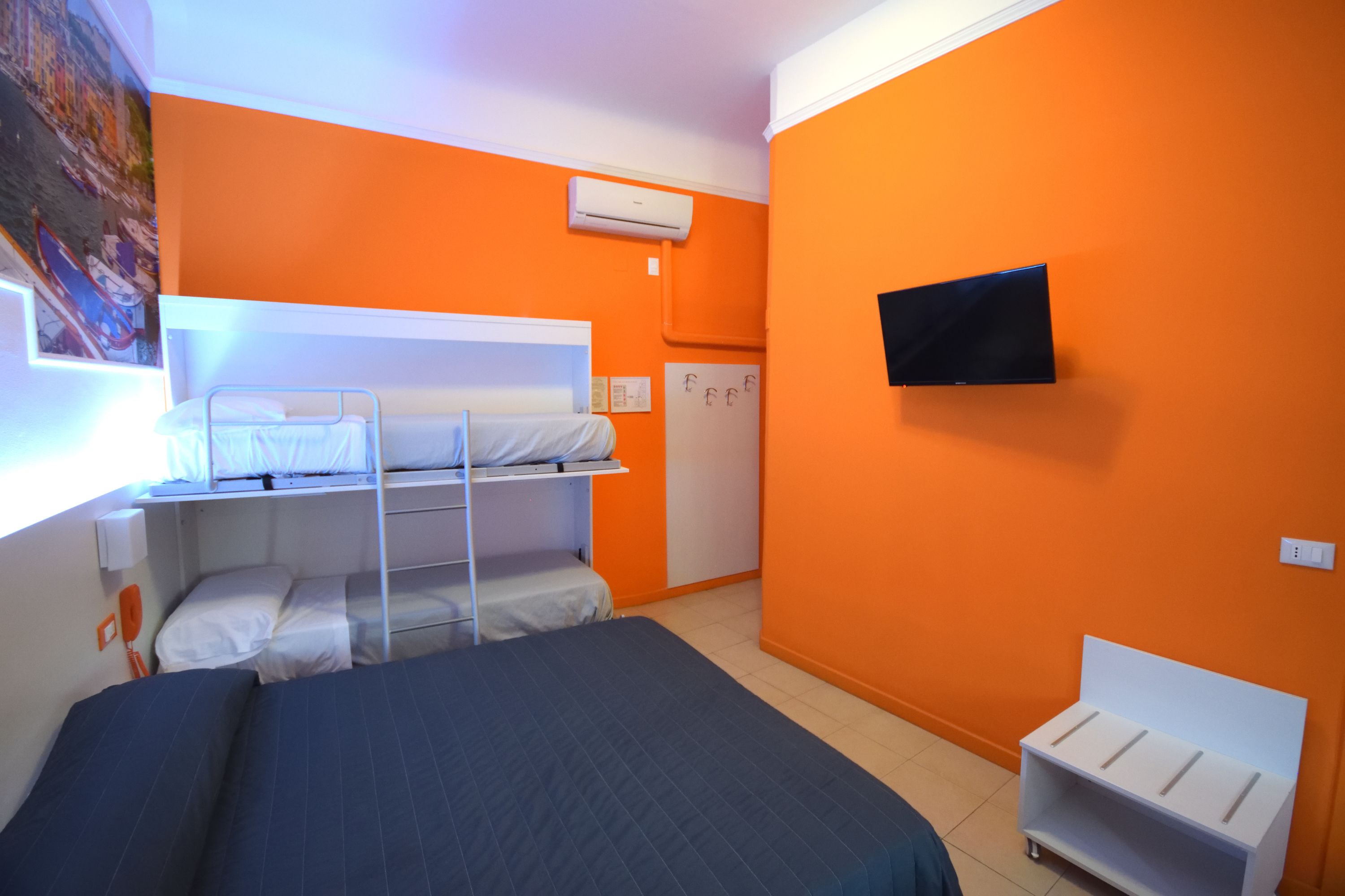 A room with orange walls, a bunk bed, a flat-screen TV, and a desk with a chair.