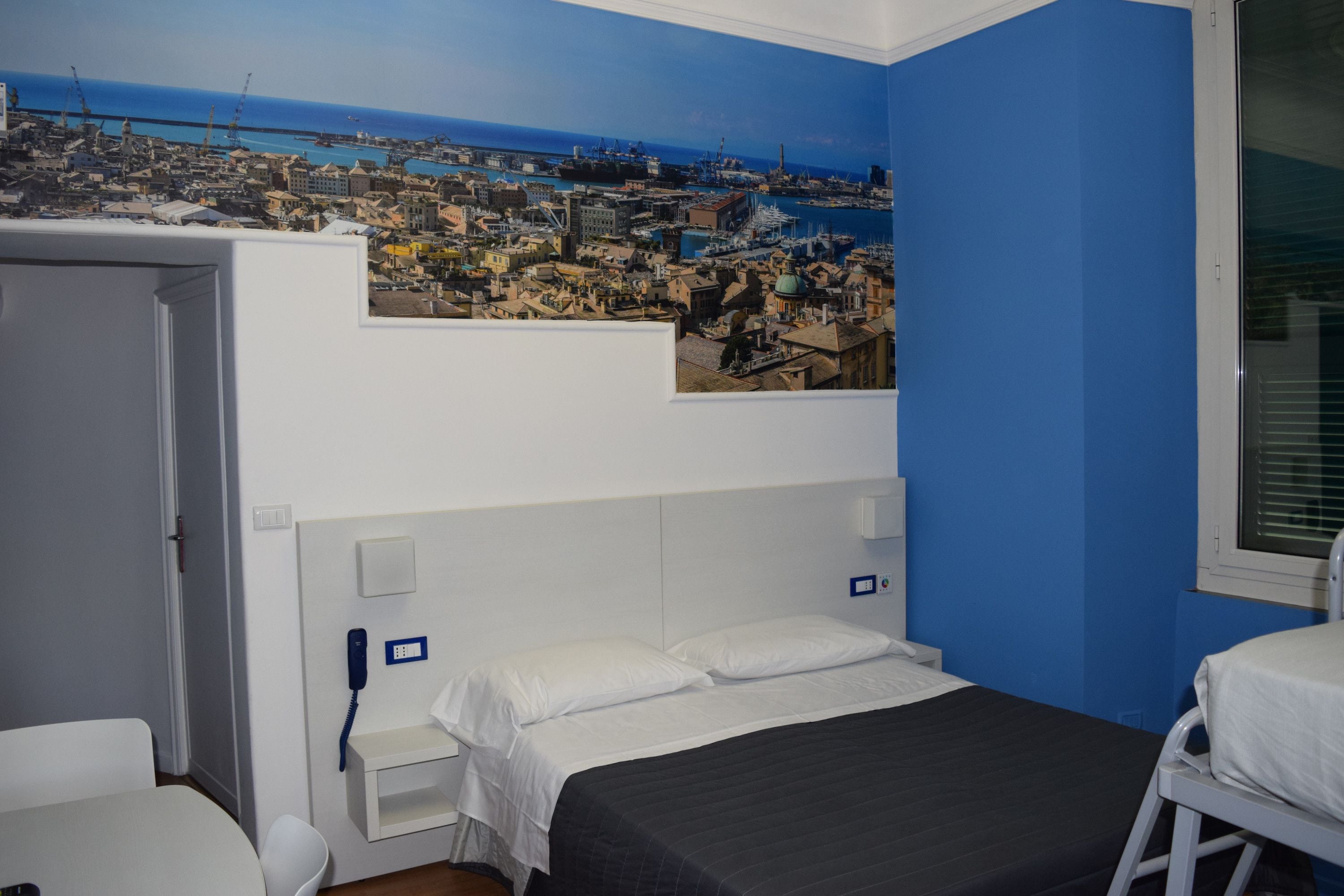 Hotelkamer met een bed, nachtkastje, telefoon en een kunstwerk aan de muur van een stadsbeeld aan de kust.