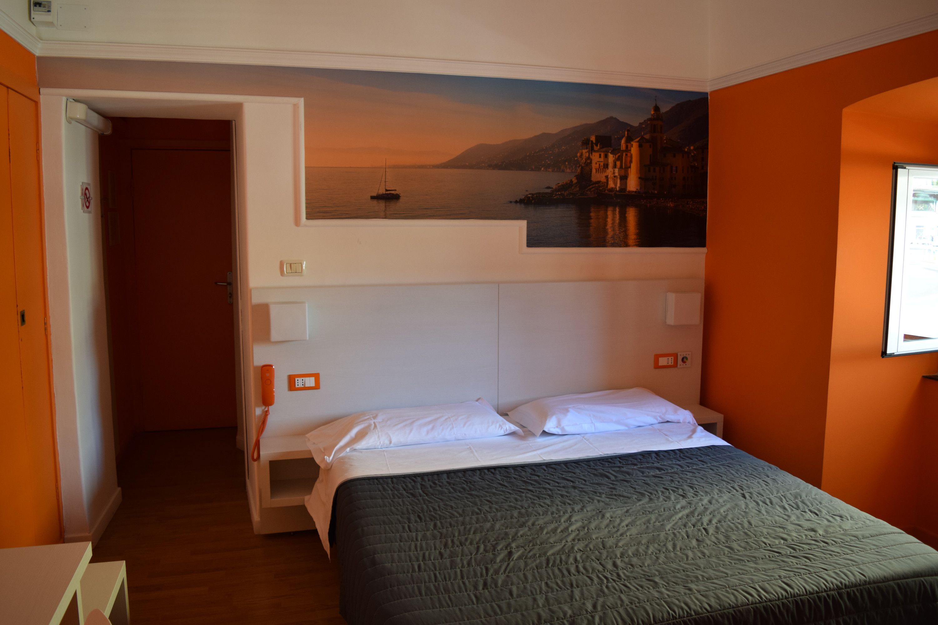 Une chambre à coucher comprenant un lit, une table de chevet, un téléphone fixé au mur et un tableau représentant un paysage côtier.