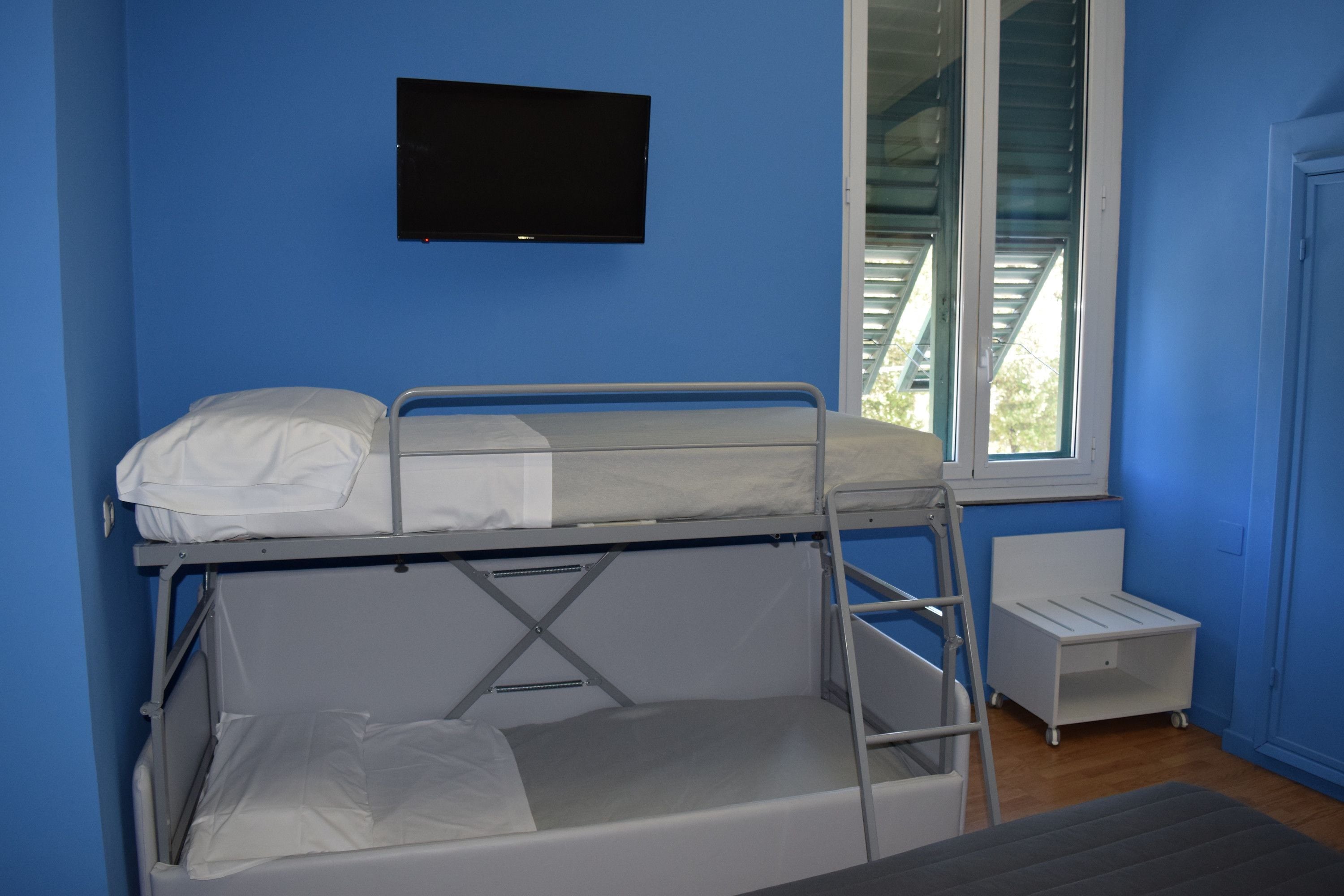 Una camera con un letto a castello, una TV montata a parete, una finestra con persiane e una piccola scrivania.