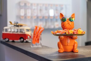 A toy cat figurine with sunglasses holding a plate of fruit.