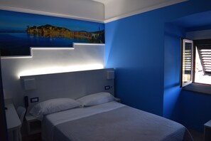 Een slaapkamer met een bed, nachtkastje, wandlamp en raam met jaloezieën.