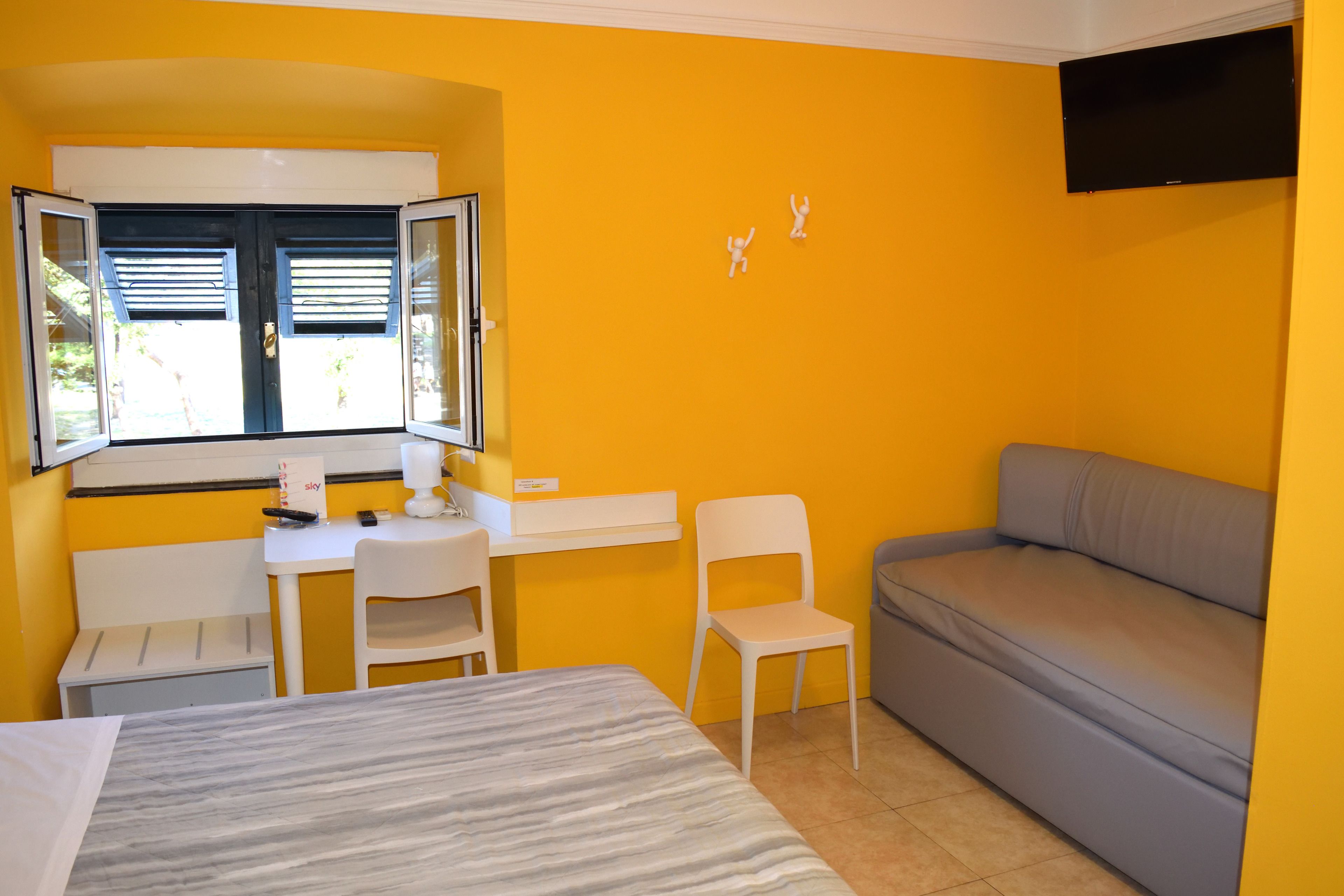 Une pièce comprenant un lit, un bureau avec une chaise, un canapé et une fenêtre avec des stores.