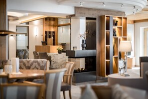 A modern living room with a fireplace, wooden shelving, and a dining area with marble tables and chairs.